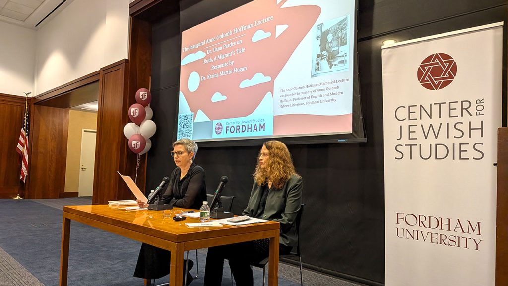 Two women seated at a table with microphones in front of them