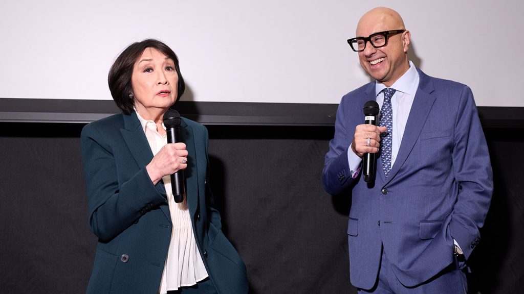 A woman speaks with a man while both hold microphones