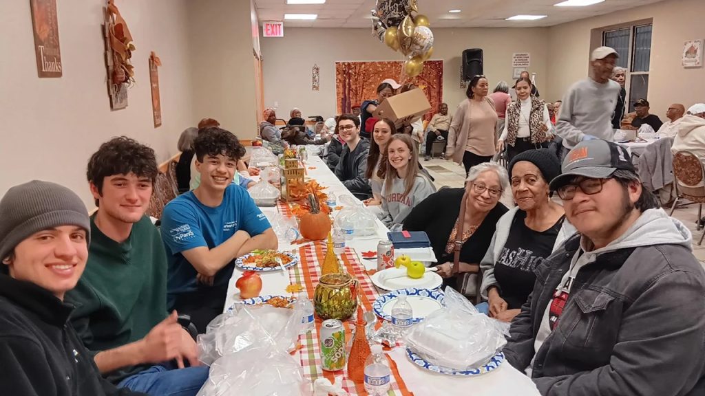 Students join senior citizens at a Thanksgiving dinner at a long table