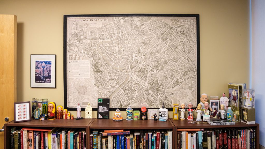 A framed map of Rome on a wall above a bookshelf