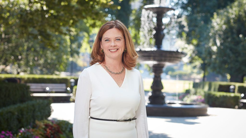 Fordham President Tania Tetlow in white dress in front of fountain