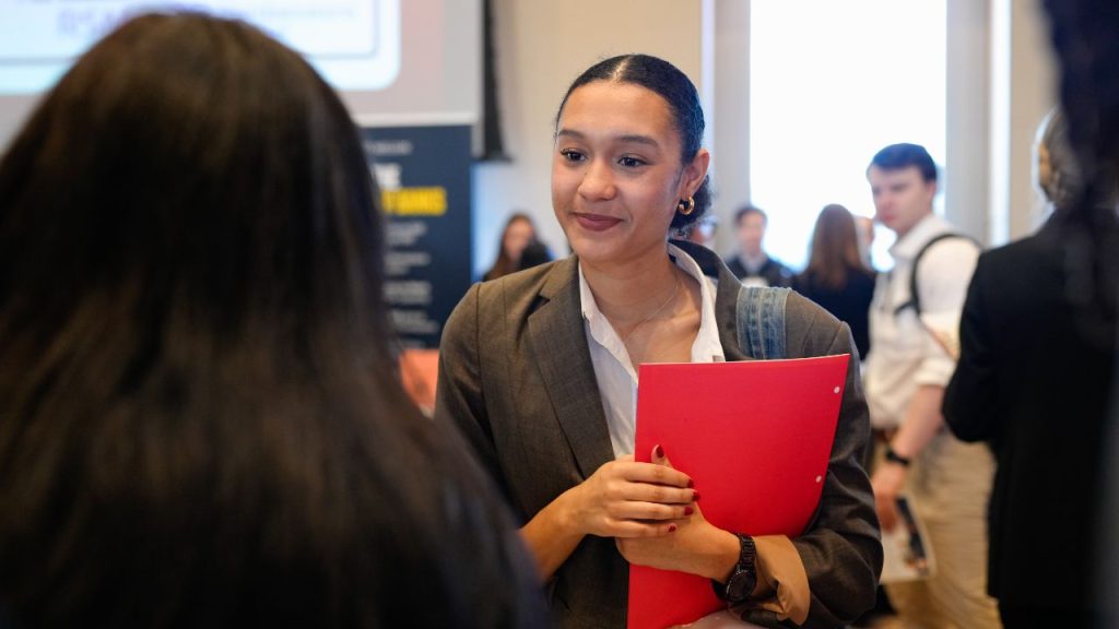 A woman with a red folder talks with another woman representing Fordham's career center
