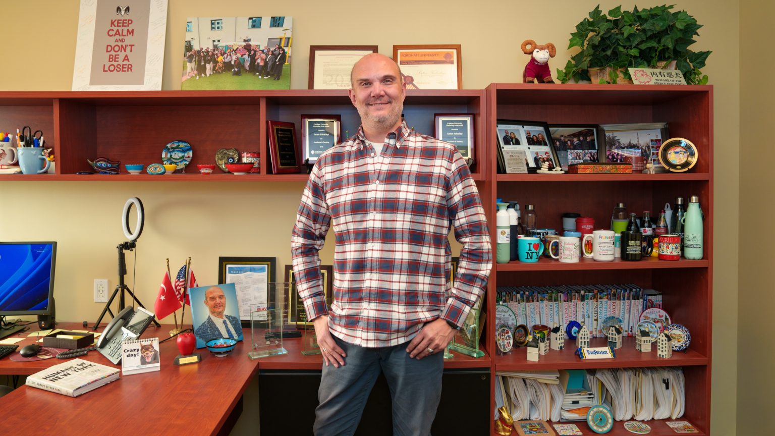 Sertan Kabadayi standing and smiling at the camera in the middle of his office in front of his desk