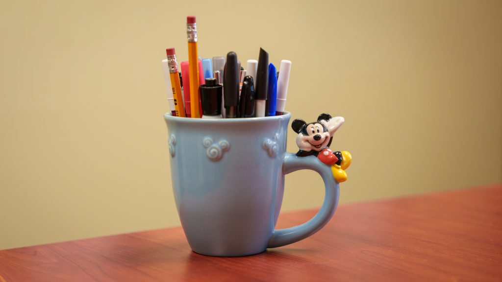 A mug with a Mickey Mouse figurine filled with pens and pencils